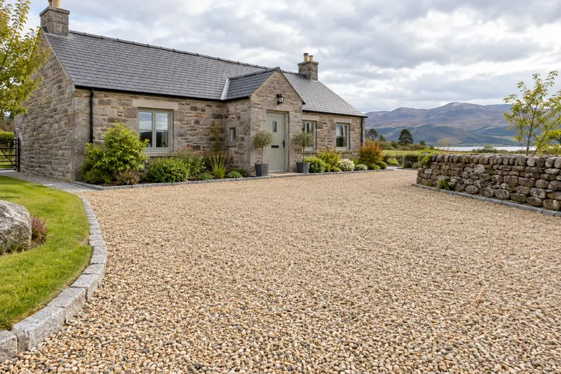 Golden gravel driveway with stone edging beside a rural Scottish cottage